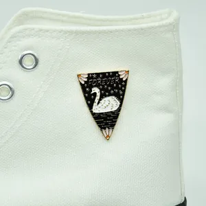 Detail of a black enamel swan brooch with FOREVER text pinned on a white canvas shoe