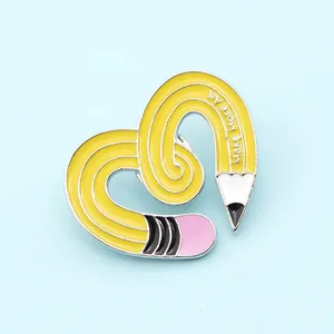 Close-up of yellow pencil heart enamel pin with Make More Art text engraving