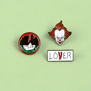Detailed view of Pennywise clown, paper boat and LOSER enamel pins set on a green surface