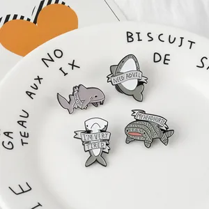 Set of four cartoon enamel shark pins with humor phrases displayed on a ceramic dish