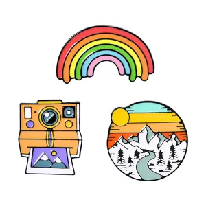 Three-piece enamel pin set featuring rainbow, vintage camera, and mountain scenery badge