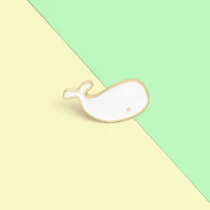 Cute white enamel whale brooch with gold edges on a minimalist pastel background