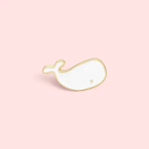 Cute white enamel whale brooch with gold trim on a soft pink background for bags