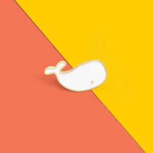 Close-up of a white whale enamel brooch with gold outlines on a vibrant dual-color background