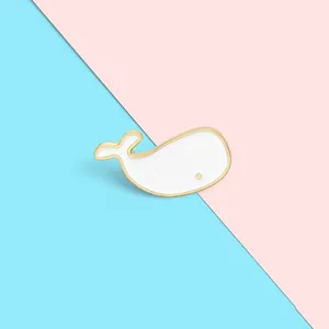 Detail of cute white whale brooch with gold enamel finish on blue and pink background