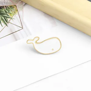 Detailed view of a cute white whale enamel pin with gold plating on a minimalist background