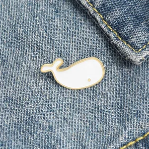 Detail of cute white and gold whale enamel pin attached to blue denim fabric