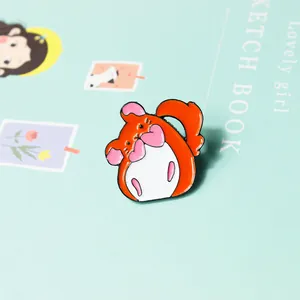 Vue détaillée d'une jolie broche hamster en émail orange sur un carnet de croquis vert