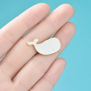 Cute white enamel whale brooch pin with gold trim, held against a blue sky background