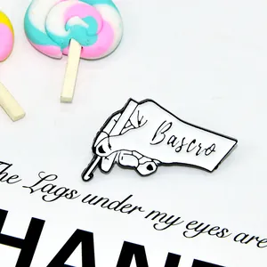 Creative white enamel pin featuring a hand holding a crochet hook with Bascro logo