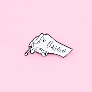 Detailed view of hand-holding crochet hook enamel pin with Bascro text on pink background