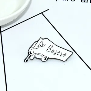 Close-up of a white enamel hand-holding pen brooch pin with black metallic outlines