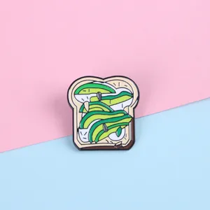 Broche en émail toast à l'avocat pour vêtements et sacs sur un fond pastel bicolore