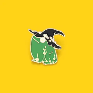 Detailed close-up of a green witch frog enamel pin with a black hat on yellow background