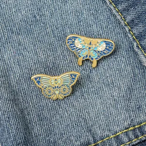 Celestial blue butterfly enamel pins with moon and star patterns on denim background