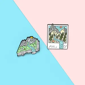 Detail of enamel pins featuring mountain landscapes in book and polaroid frame shapes
