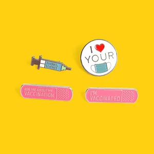 Set of four colorful enamel lapel pins with vaccine and mask themes on a yellow background