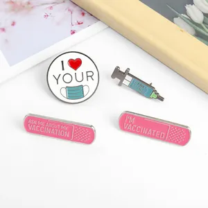 Detail of four medical enamel pins featuring a mask, syringe, and pink bandages on white