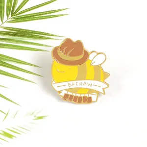 Macro detail of enamel bee pin wearing a cowboy hat with Beehaw text and gold plating
