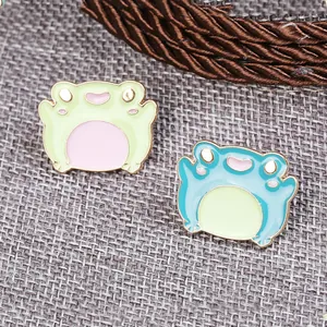Set of two cute cartoon frog enamel pins in green and blue colors with metallic edges