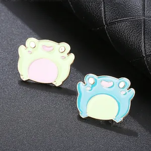 Detail of green and blue cartoon frog enamel pins with polished gold edges on dark leather