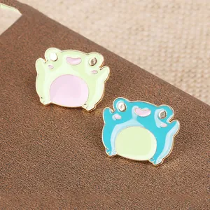 Detailed close-up of cute cartoon frog enamel pins in green and blue with gold edges