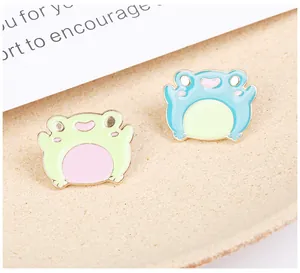 Detail shot of cute cartoon frog enamel pins in green and blue colors on a beige tray