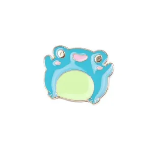 Detailed view of a cute blue enamel frog pin with a gold metal edge and smiling face