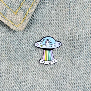Detailansicht der Einhorn UFO Emaille-Anstecknadel mit Regenbogen auf Denim-Stoff