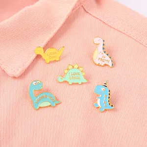Vue détaillée du lot de 5 pins dinosaures en émail sur un fond en tissu denim rose