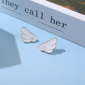 Close-up of white angel wing stud earrings with gold trim on a minimalist background