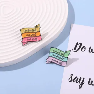 Détail de pins en émail avec dégradé et phrases motivantes sur un plateau ondulé