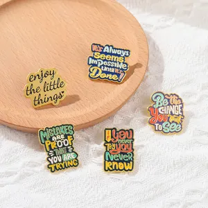 Detail of five vintage enamel pins with motivational quotes on a rustic wooden tray