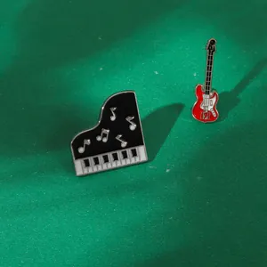 Dettaglio delle spille smaltate a forma di pianoforte e chitarra su sfondo verde