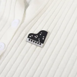 Dettaglio di una spilla a pianoforte vintage in smalto su un maglione bianco a coste fini
