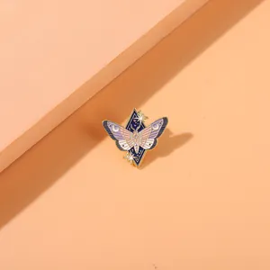 Detailed enamel moth brooch with moon and star accents on a blue diamond-shaped base