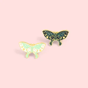 Detailed macro of two enamel butterfly pins featuring artistic moon phase wing patterns