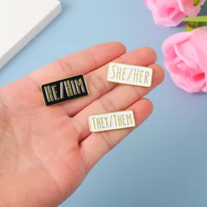 Dreiteiliges Emaille-Pronomen-Pins-Set mit He, She, They Schriftzug in Goldrahmen