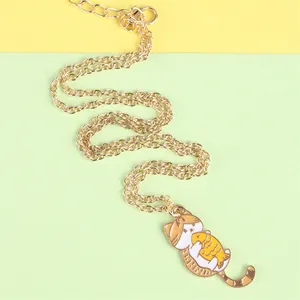 Close-up of golden chain necklace with cartoon cat holding fish pendant on bright paper