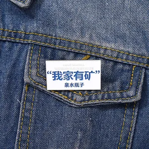 Detailed view of rectangle enamel pin with humorous text pinned to denim jacket pocket