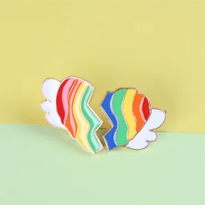 Detail van hart-emaille broche met regenboogstrepen en witte vleugels op goudkleurig metaal