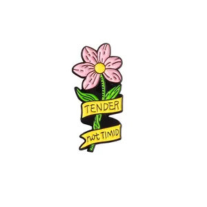 Dettaglio della spilla in smalto a fiore con petali rosa e nastro con scritta TENDER not TIMID