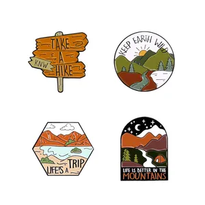 Detailed close-up of four outdoor enamel pins showing mountains and hiking slogans