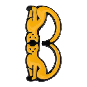 Detail of creative enamel pin showing two yellow cats forming the letter B shape