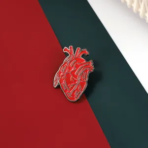 Macro detail of anatomical red heart enamel pin showing realistic aorta and ventricle text