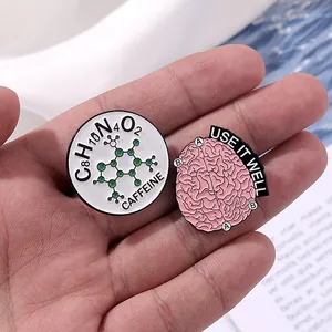 Detail of caffeine molecule and pink brain enamel pins held by hand on creative background