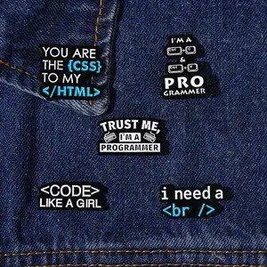 Detailed close-up of five unique programmer-themed enamel brooches on blue denim fabric