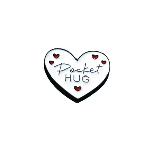 Detail van een witte hartvormige Pocket Hug-badge met rode hartjes en artistieke zwarte tekst