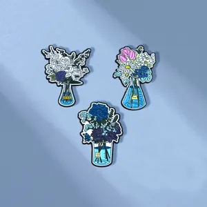 Three creative enamel pins featuring floral bouquets in lab beakers and flasks