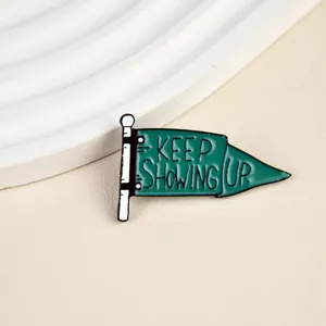 Close-up of green flag enamel pin with Keep Showing Up text on textured beige surface